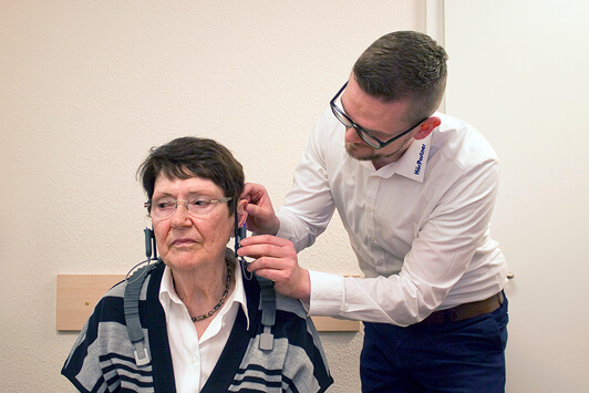 Ein Hörakustiker passt einer Seniorin ein Hörgerät zur Hörtest-Diagnose an.