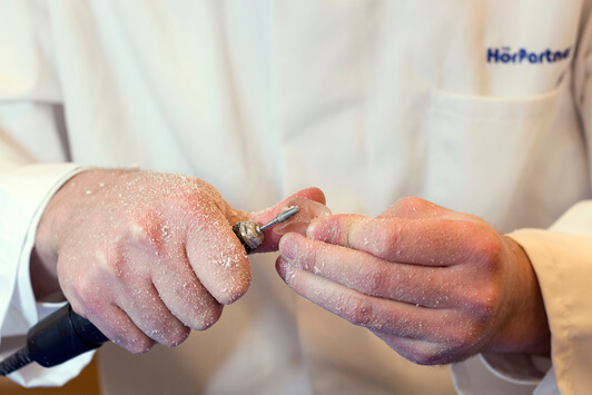 Ein Akustiker bearbeitet ein Hörgerät mit einem Fräswerkzeug in der Werkstatt.